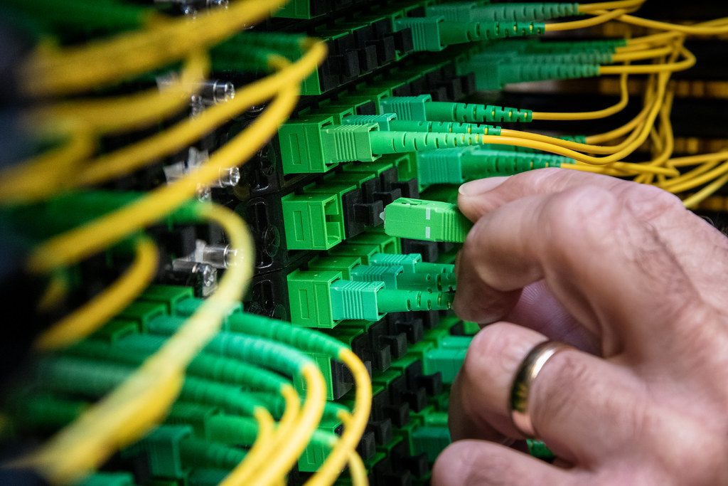 Hands terminating optical fibre connectors on a green patch panel